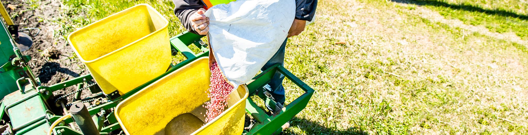 Man pouring seeds into a tractor planter attachment