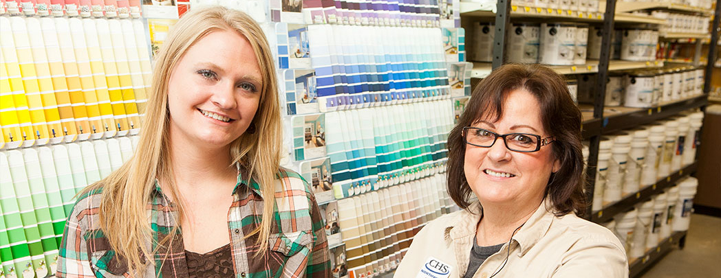 Two women standing beside a paint sample wall in a hardware store