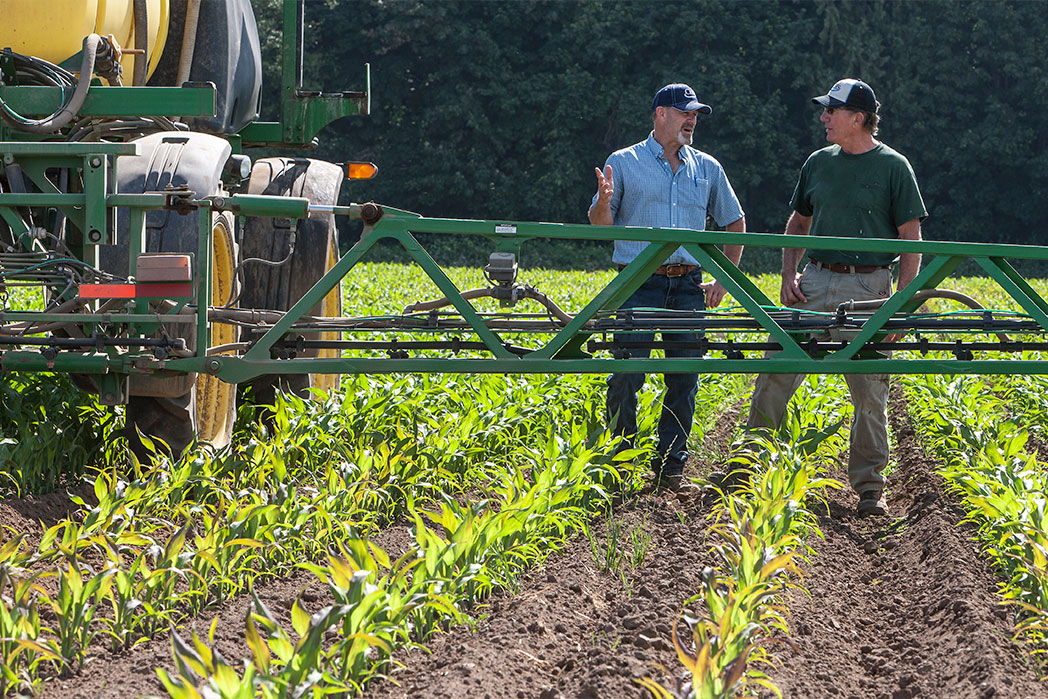 Two men standing beside a tractor sprayer attachment