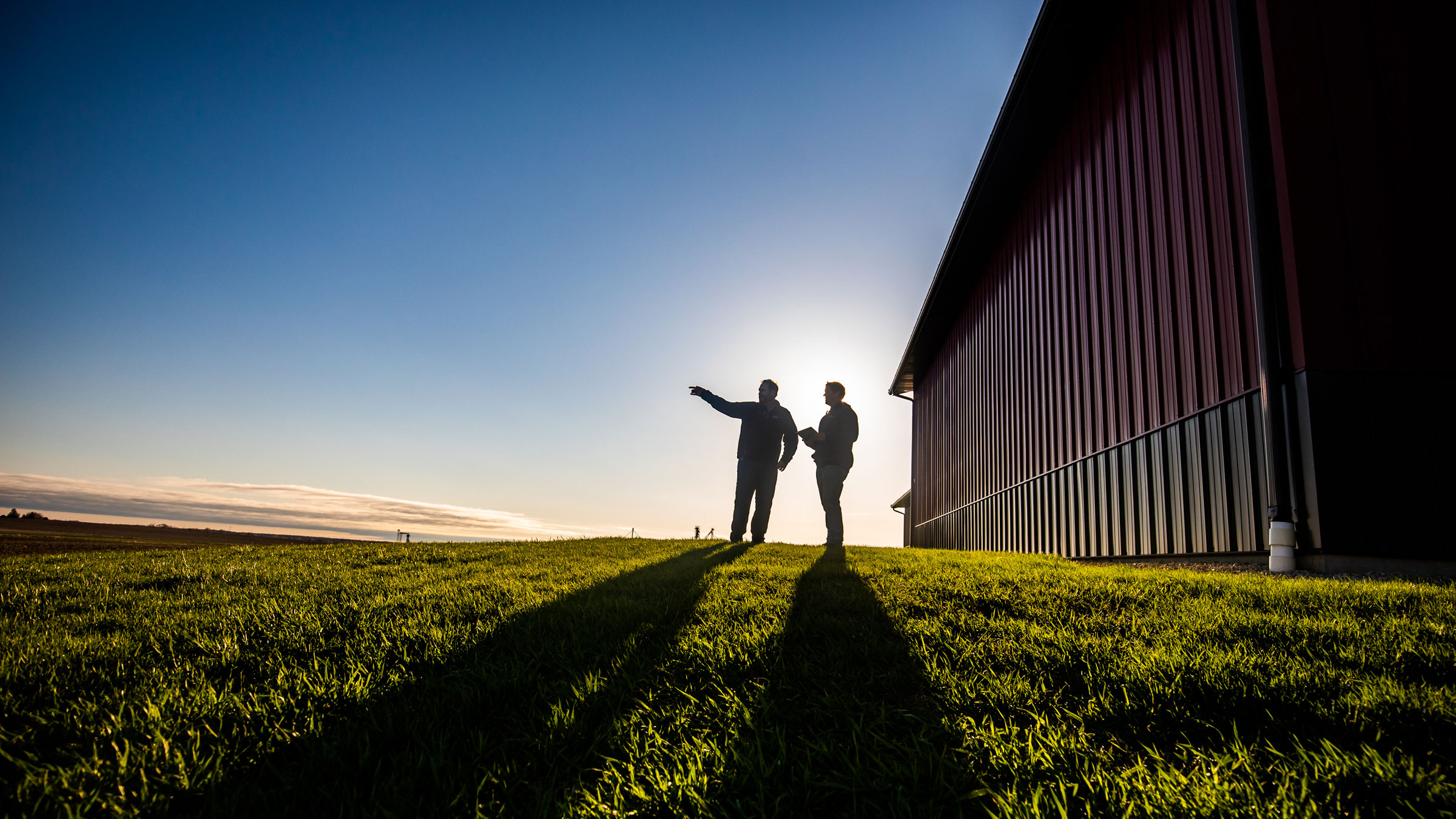 Two men standing beside a barn at dusk